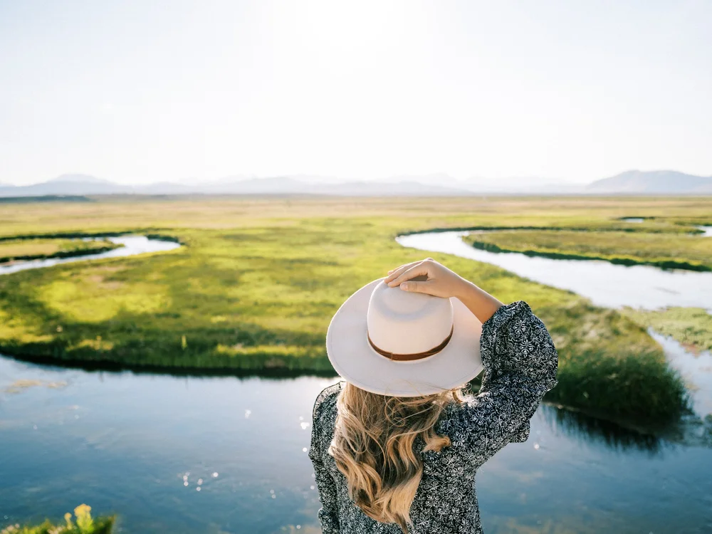 A woman in a wide-brim hat looking out over a green marsh