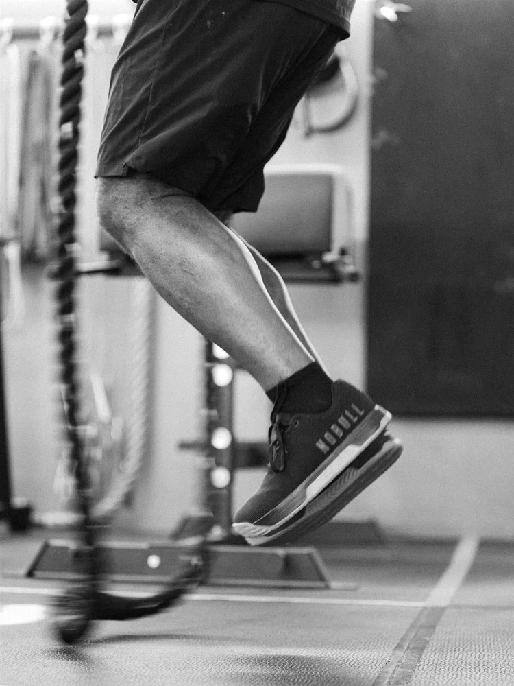 A black-and-white frame of an athlete training with battle ropes