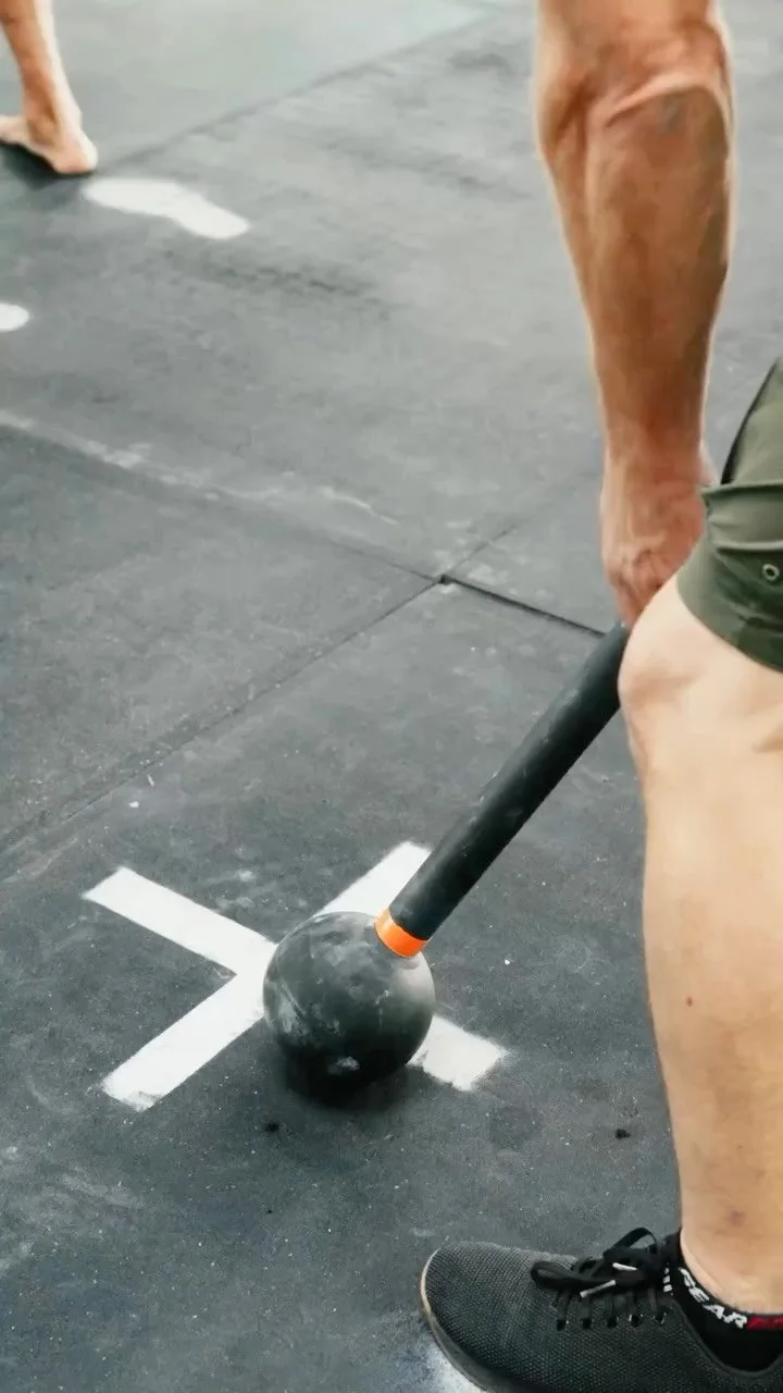 An athlete standing over a steel mace on a concrete training pad