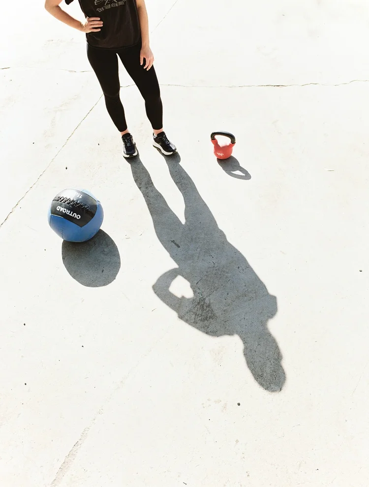 An overhead frame of an athlete's shadow beside a kettlebell and medicine ball
