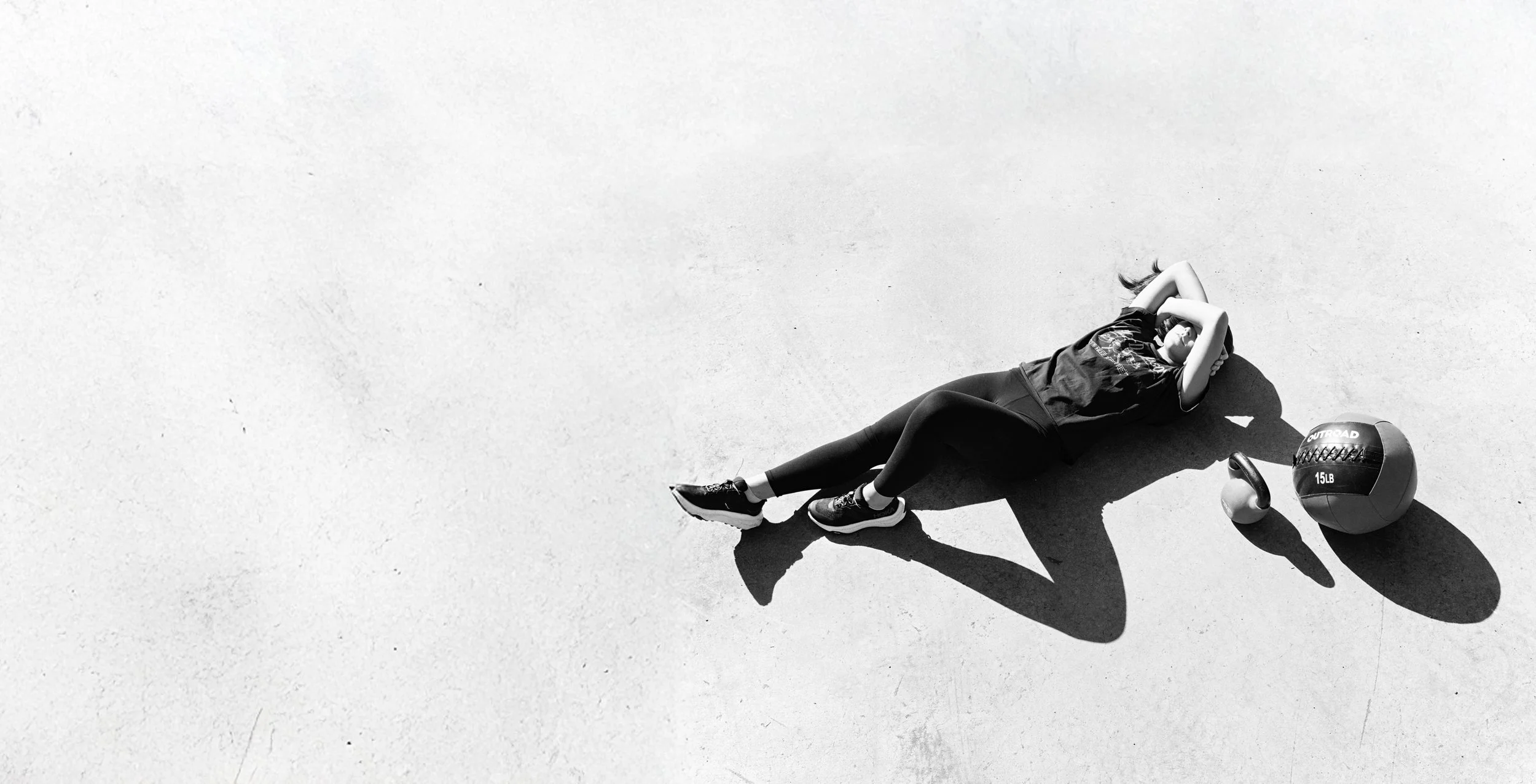 An overhead black-and-white photograph of an athlete in a push-up position beside a medicine ball