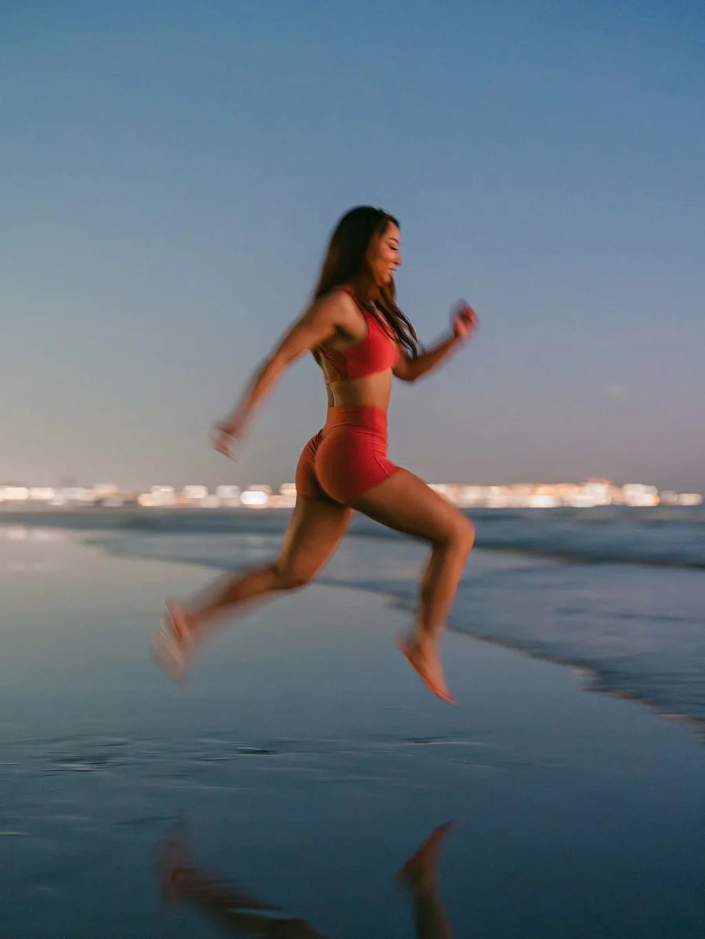 A runner striding through shallow water along the shoreline at sunset
